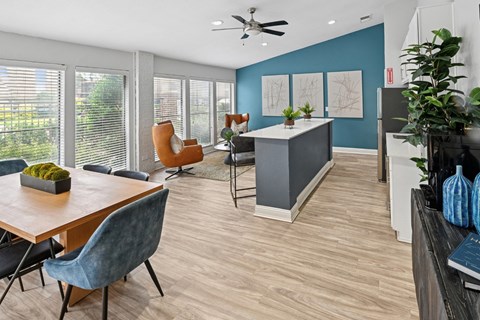 A modern clubhouse with comfortable seating, a ceiling fan, kitchen, and wood floors at Estelle Creek North Apartments in Irving, TX